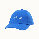 A bright blue baseball cap with 'Detroit' embroidered in white script on the front, shown against a plain off-white background.