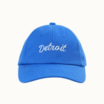 A bright blue baseball cap with 'Detroit' embroidered in white script across the front, shown against a plain off-white background.