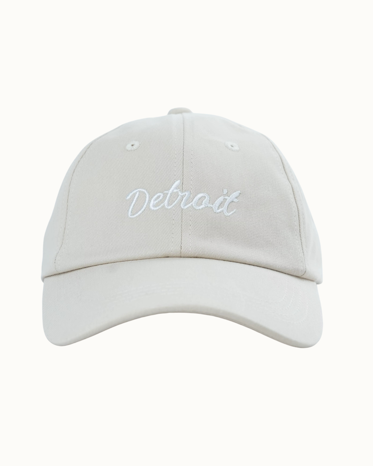 A light beige baseball cap with 'Detroit' embroidered in white script across the front, shown against a plain off-white background.